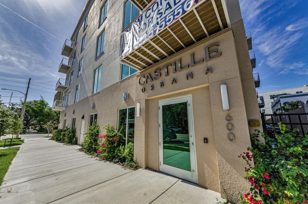 The exterior of a multi-story apartment building features a glass entrance door and signage — 600 3RD AVENUE S UNIT 301, ST PETERSBURG, FL