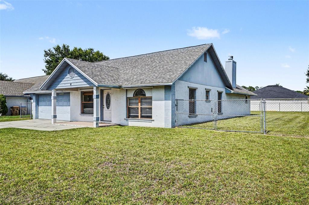 A single-story house with a light-colored stucco exterior, a gray roof, and a chain-link fence — 4 CARMONA WAY, KISSIMMEE, FL