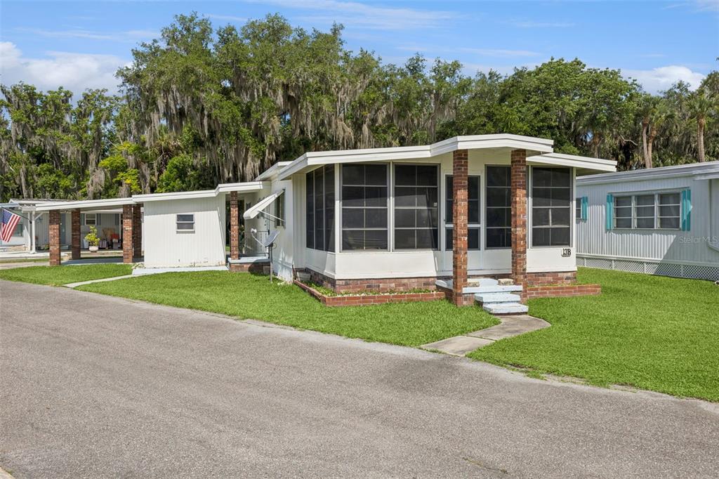 A single-story manufactured home features a screened-in front porch with brick pillars and a carport — 13 COCOS PLUMOSA DRIVE UNIT B, EUSTIS, FL