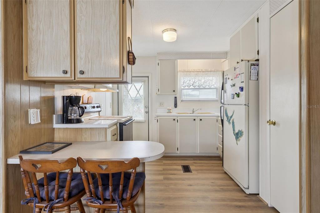 A kitchen with wood-paneled walls, white cabinets, a breakfast bar, and wood-look flooring — 13 COCOS PLUMOSA DRIVE UNIT B, EUSTIS, FL