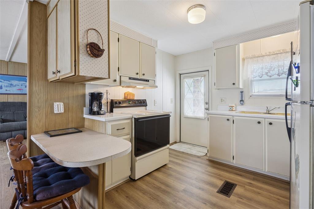 A kitchen with light-colored cabinets, a small breakfast bar, and wood-look flooring — 13 COCOS PLUMOSA DRIVE UNIT B, EUSTIS, FL