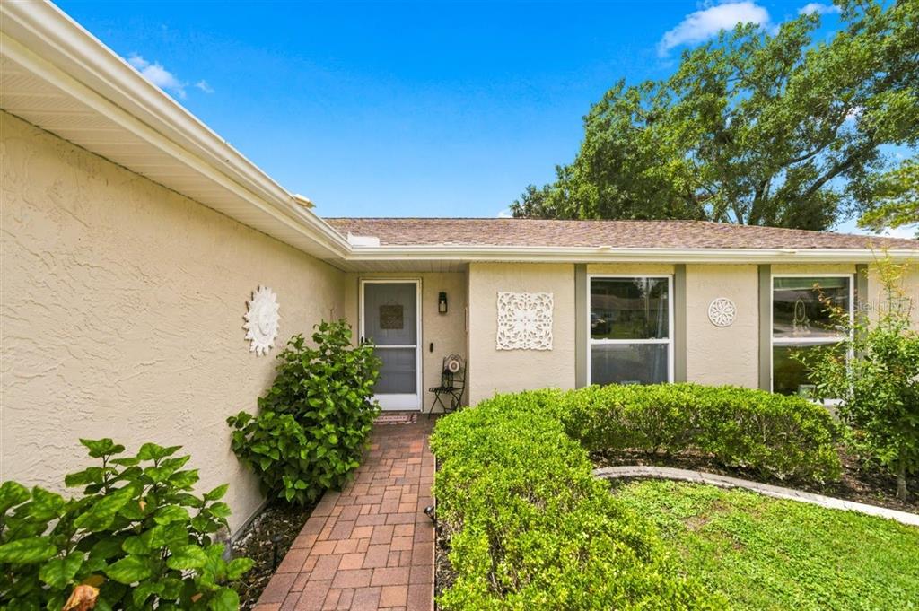 A brick walkway leads to the front entrance of a single-story home with beige stucco — 5309 BLACK PINE DRIVE, TAMPA, FL
