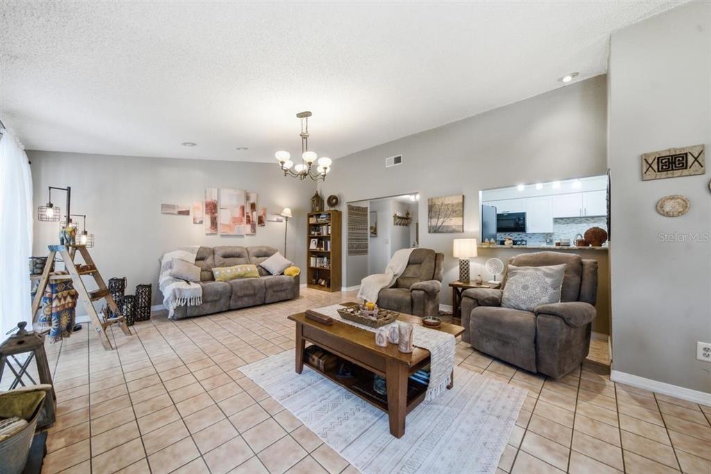 A living room features tile floors, a vaulted ceiling, a chandelier, and a pass-through kitchen — 5309 BLACK PINE DRIVE, TAMPA, FL