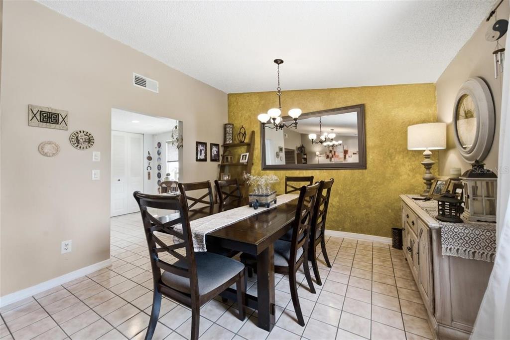 A dining room features a dark wood table, chairs, a gold accent wall, and tiled floors — 5309 BLACK PINE DRIVE, TAMPA, FL