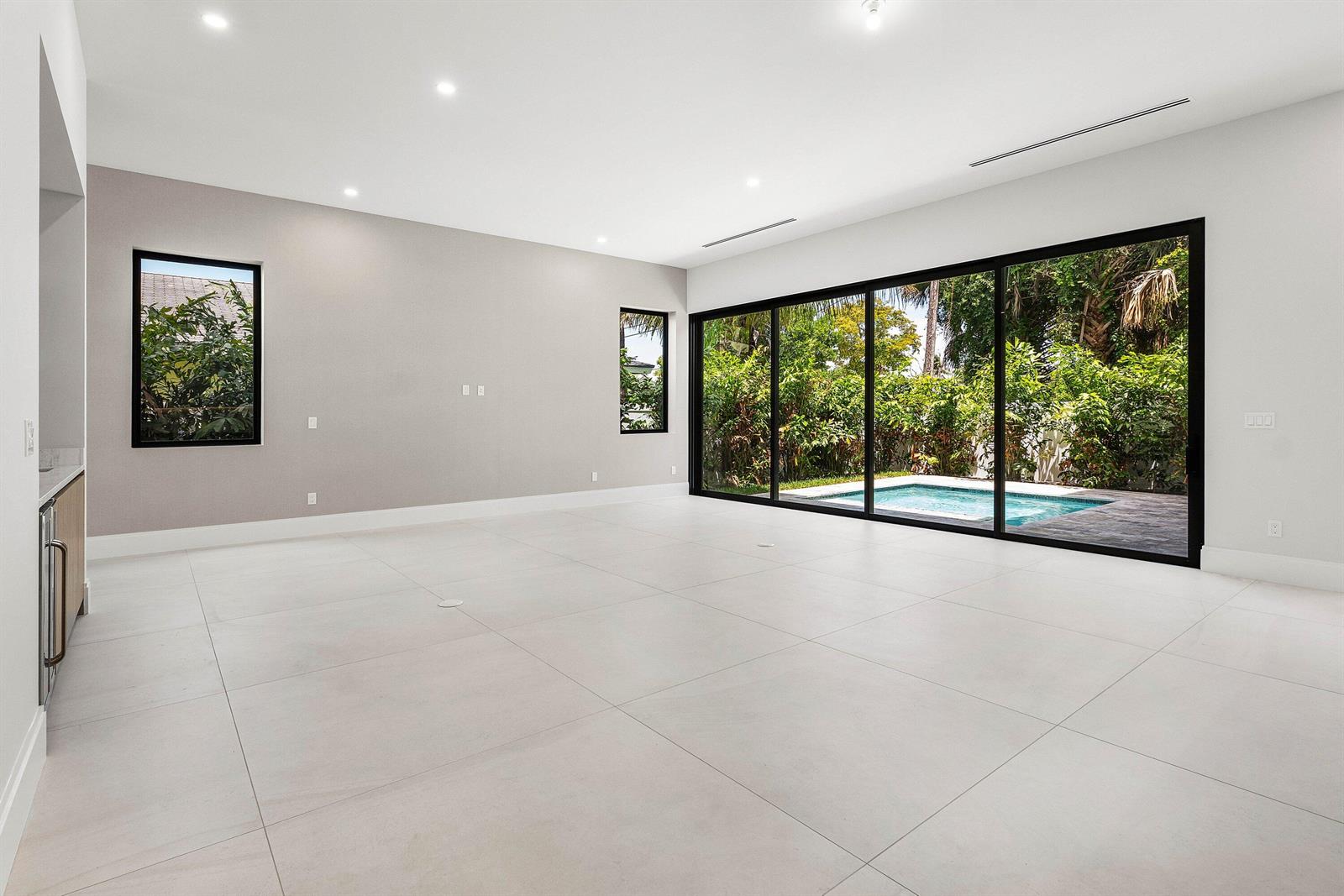 A minimalist living area features large light-colored floor tiles, grey walls, and sliding glass doors — 207 SE 5th Street, Delray Beach FL 33483, DELRAY BEACH, FL
