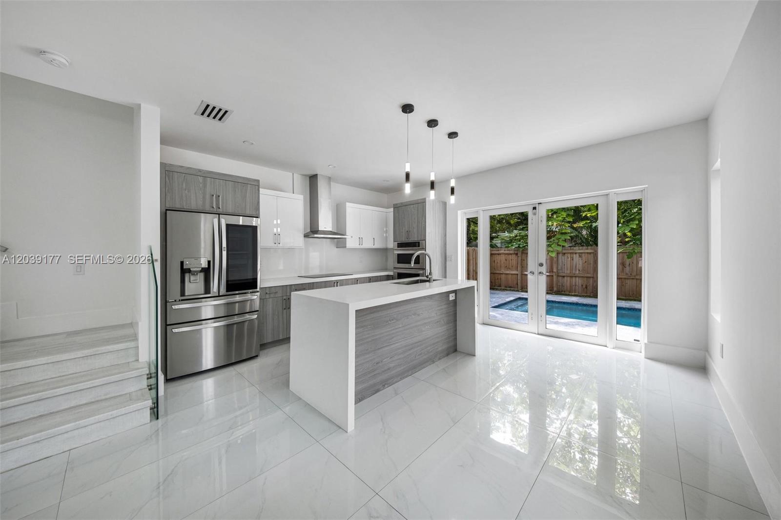A modern kitchen features white marble floors, two-toned cabinetry, a waterfall island, and glass doors — 3142 Carter St # 3142, Miami FL 33133, MIAMI, FL