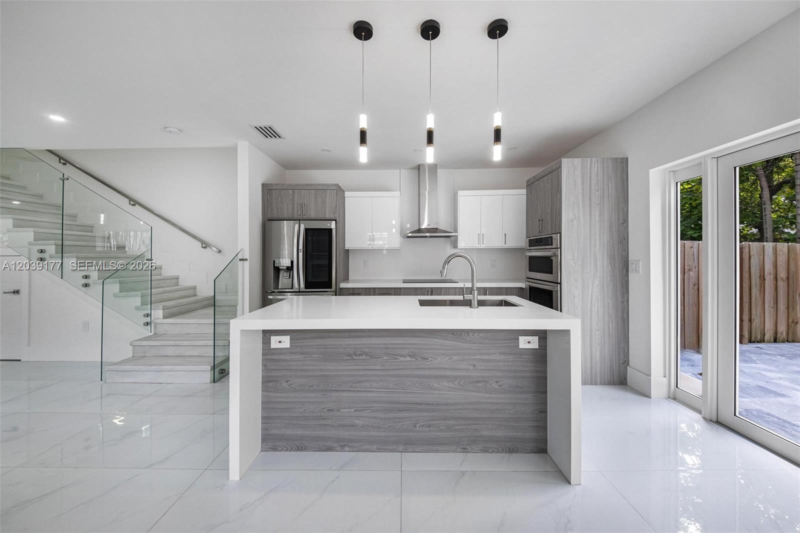 A modern kitchen features a waterfall island, gray wood-grain cabinetry, and a glass-railed staircase — 3142 Carter St # 3142, Miami FL 33133, MIAMI, FL