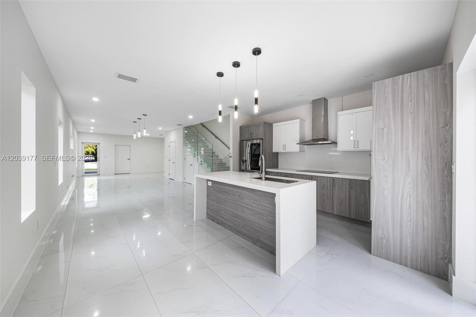 A modern kitchen features a white waterfall island, gray wood-grain cabinetry, and white tile flooring — 3142 Carter St # 3142, Miami FL 33133, MIAMI, FL