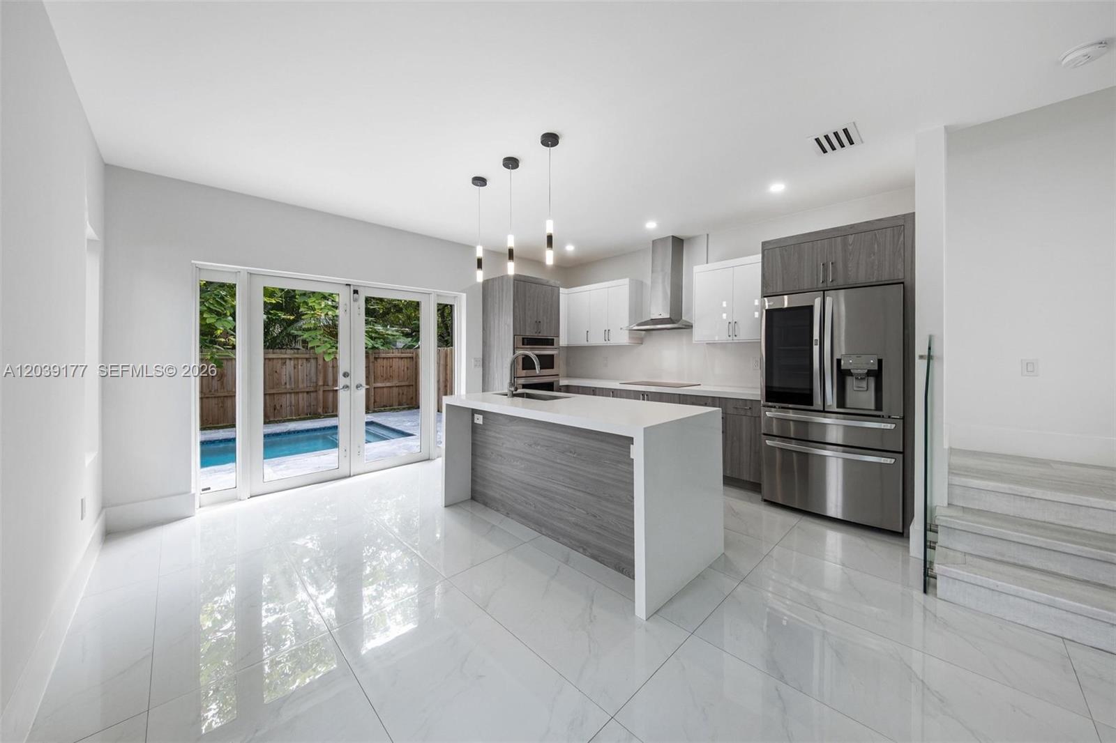 A modern kitchen features a central island, stainless steel appliances, and white marble-style flooring — 3142 Carter St # 3142, Miami FL 33133, MIAMI, FL