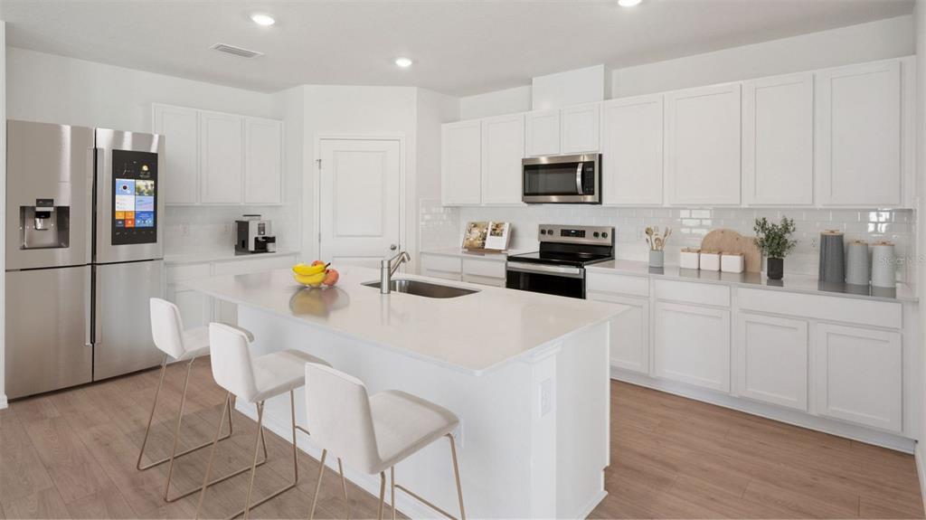 A modern kitchen features white cabinetry, stainless steel appliances, a center island, and wood flooring — 1124 MORFONTAINE STREET, DAYTONA BEACH, FL