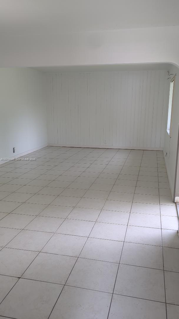 An empty room features white walls, vertical wood paneling, and light-colored square floor tiles — HOLLYWOOD, FL