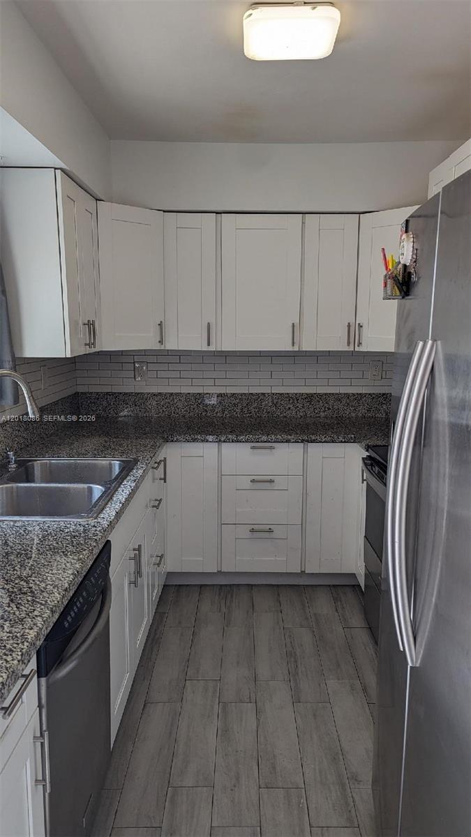 A kitchen features white cabinets, granite countertops, stainless steel appliances, and gray wood-look flooring — HOLLYWOOD, FL