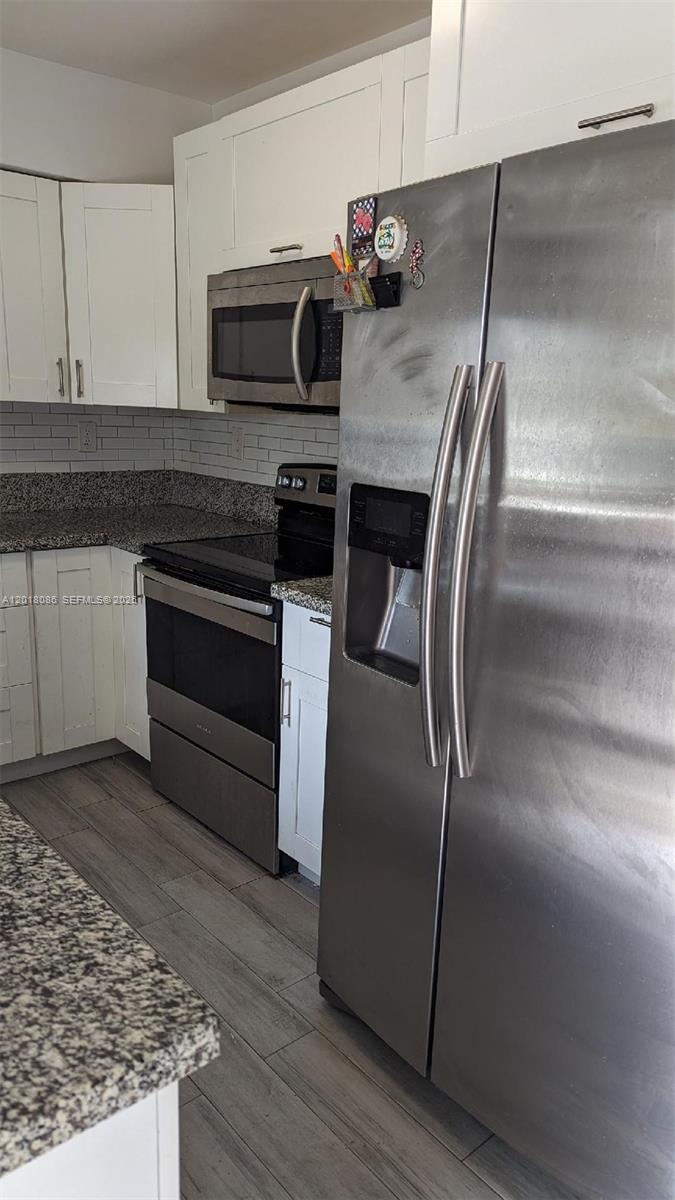 A kitchen features white cabinets, stainless steel appliances, and speckled granite countertops — HOLLYWOOD, FL