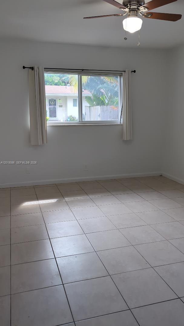 A room with white walls, light-colored tile flooring, a ceiling fan, and a window — HOLLYWOOD, FL