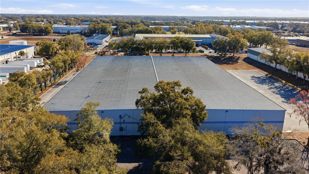 An aerial view shows a large industrial warehouse building with a metal roof and trees — 451 SW 57TH AVENUE, OCALA, FL