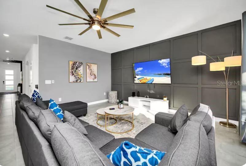 A living room features a gray sectional sofa, a dark paneled accent wall, and a ceiling fan — 9149 SOMMERSET HILLS DRIVE, DAVENPORT, FL