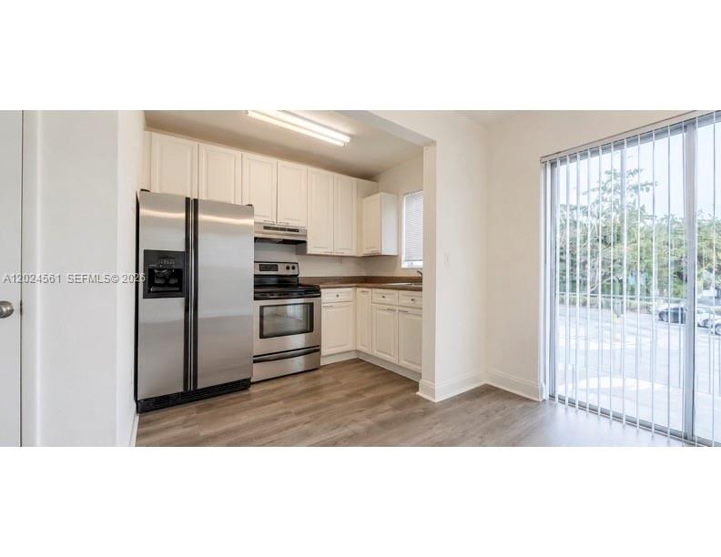 A kitchen features white cabinets, stainless steel appliances, wood-look flooring, and a sliding glass door — 5960 NE 5th Ct # 4, Miami FL 33137, MIAMI, FL