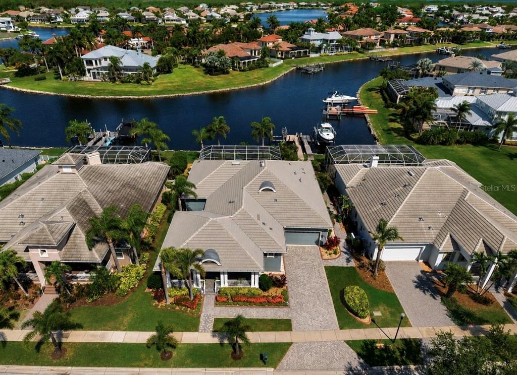 An aerial view shows three waterfront houses with tiled roofs and screened-in back lanais — 5416 MERRITT ISLAND DRIVE, APOLLO BEACH, FL