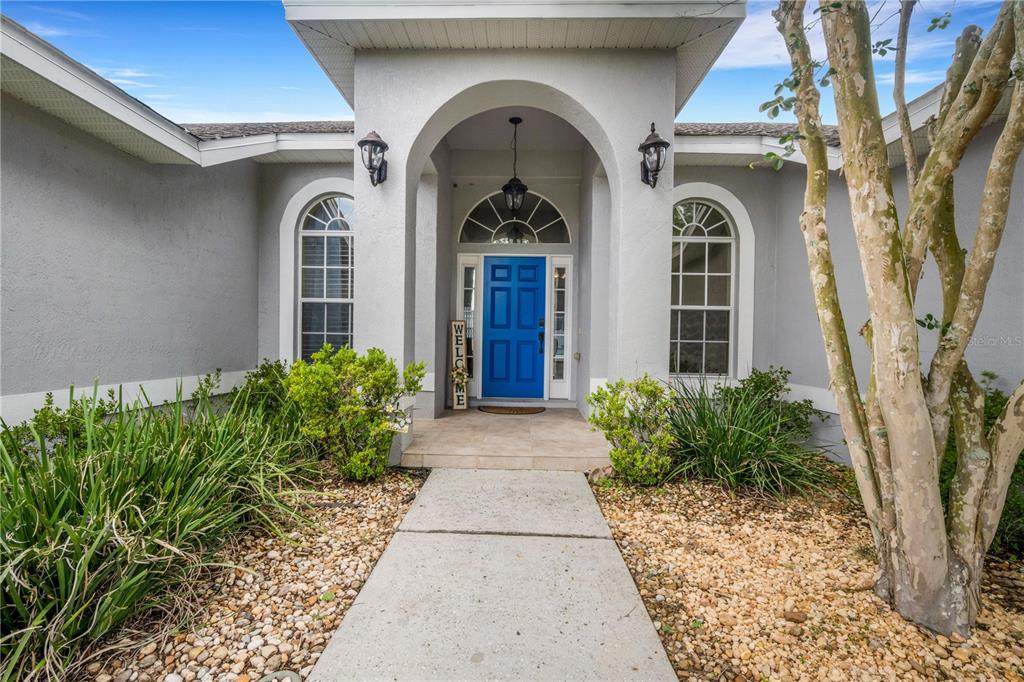 A concrete walkway leads to the blue front door of a gray stucco house — 8722 FORT SOCRUM VILLAGE PLACE, LAKELAND, FL