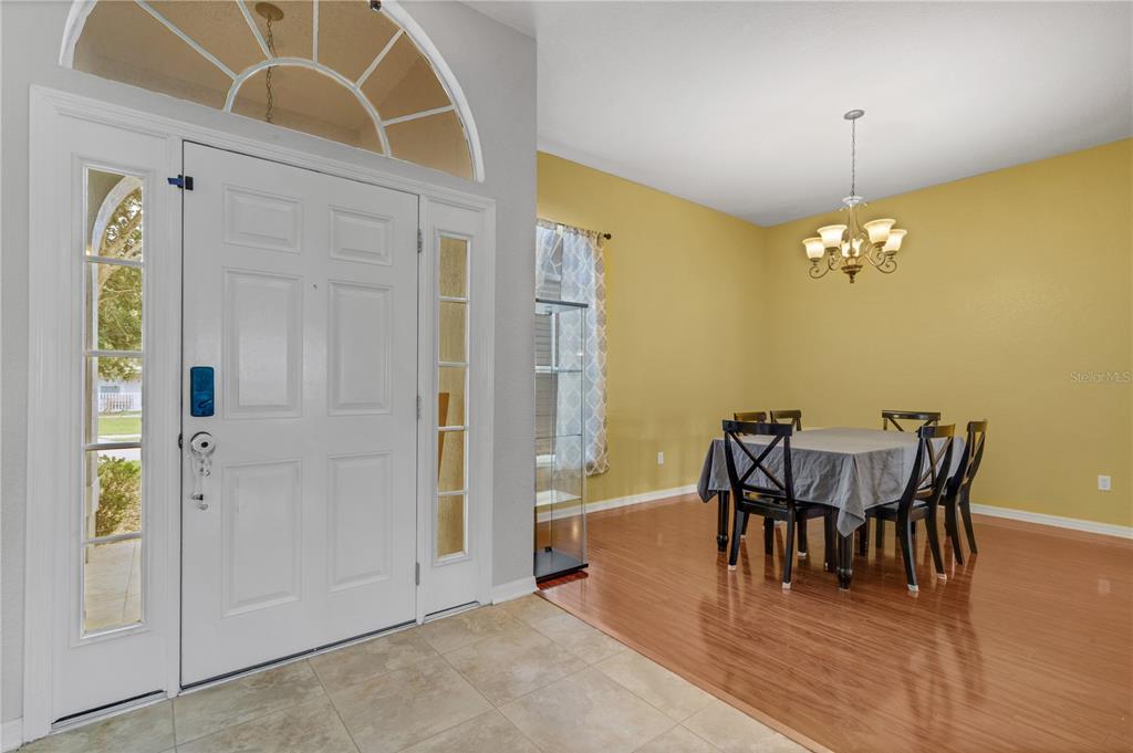 An entryway with tile flooring leads into a dining room featuring hardwood floors and yellow walls — 8722 FORT SOCRUM VILLAGE PLACE, LAKELAND, FL