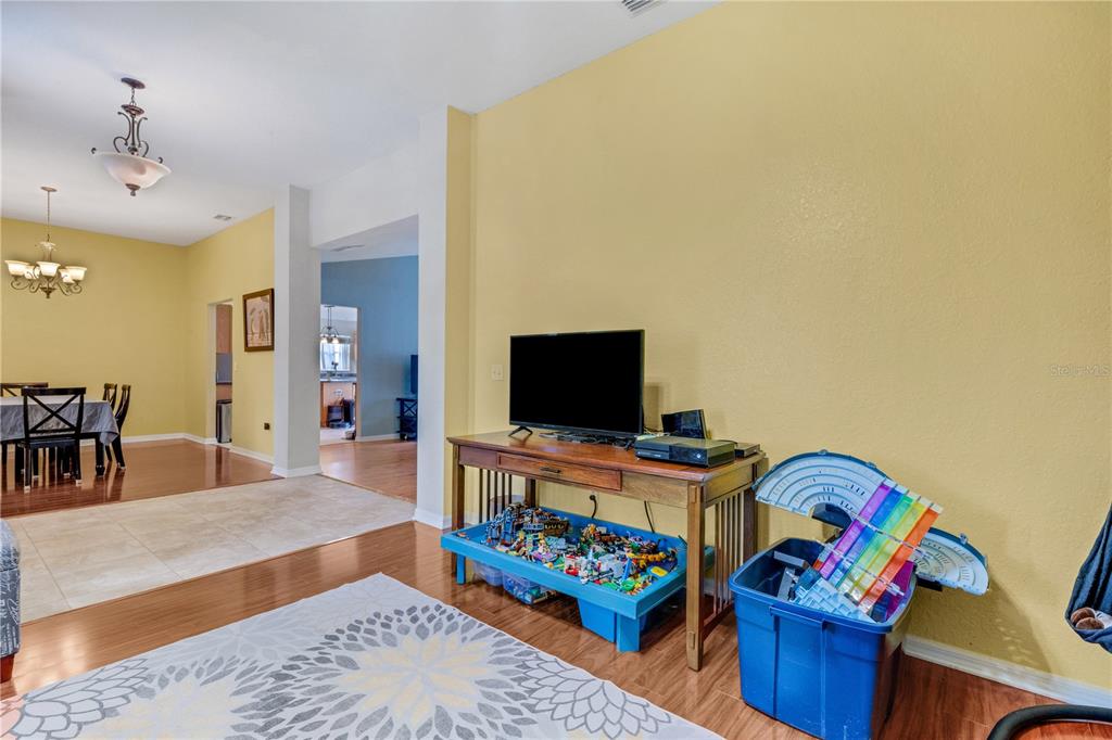 A living room with yellow walls, wood flooring, a television on a table, and toys — 8722 FORT SOCRUM VILLAGE PLACE, LAKELAND, FL