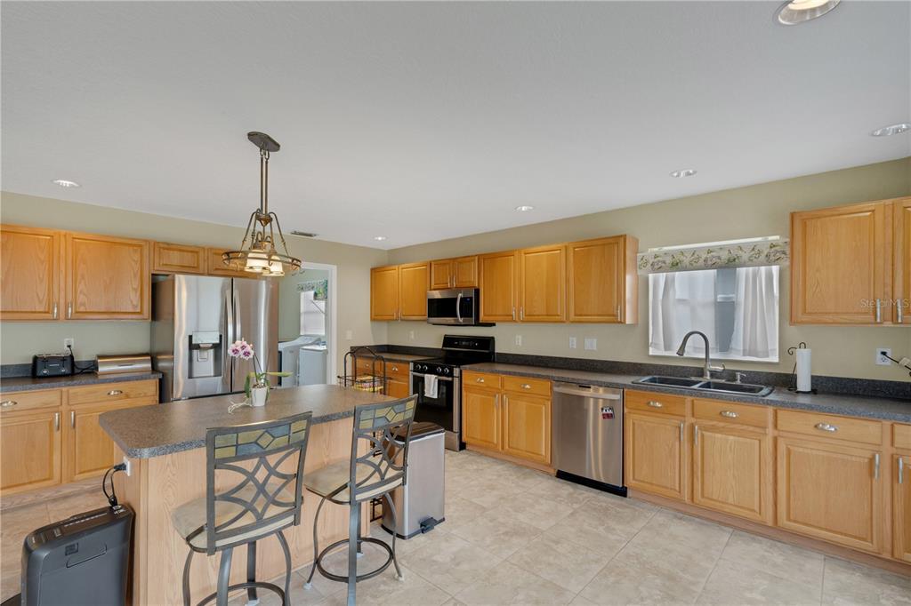 A kitchen features light wood cabinets, dark countertops, a central island, and stainless steel appliances — 8722 FORT SOCRUM VILLAGE PLACE, LAKELAND, FL