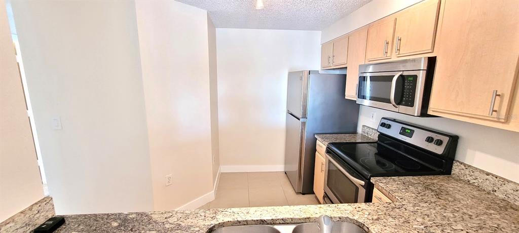 A kitchen features light wood cabinets, granite countertops, and stainless steel appliances — 3508 WINDY WALK WAY UNIT 6301, ORLANDO, FL