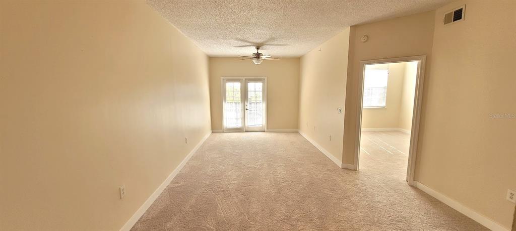 An empty living room features beige carpet, light-colored walls, a ceiling fan, and glass doors — 3508 WINDY WALK WAY UNIT 6301, ORLANDO, FL