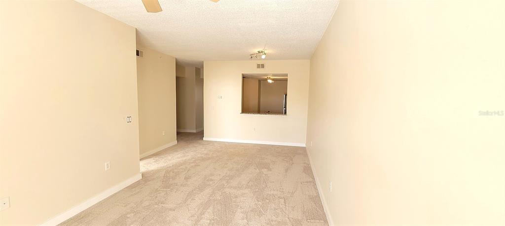 An empty living room features beige carpet, light-colored walls, and a pass-through window to the kitchen — 3508 WINDY WALK WAY UNIT 6301, ORLANDO, FL