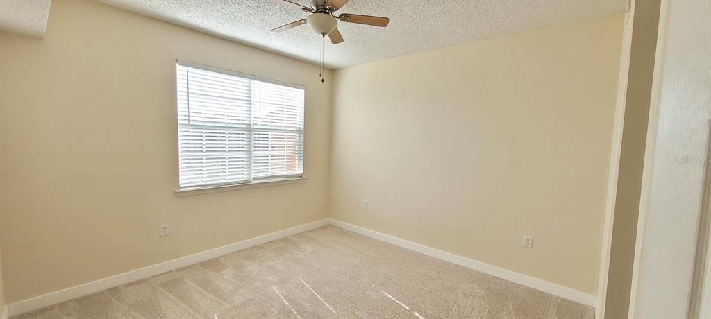 An empty bedroom features beige walls, white trim, carpeted flooring, and a ceiling fan — 3508 WINDY WALK WAY UNIT 6301, ORLANDO, FL