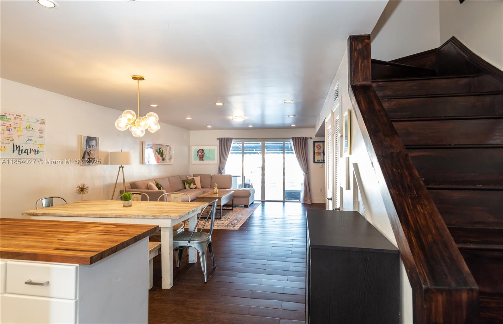An open-concept living and dining area features dark wood flooring, a wooden staircase, and sliding doors — 2035 NE 123rd St, North Miami FL 33181, NORTH MIAMI, FL