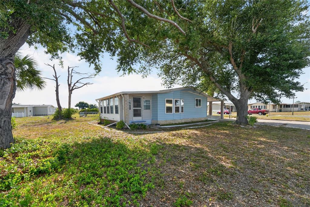A light blue mobile home sits on a grassy lot shaded by large oak trees — 6198 ORIOLE BOULEVARD, ENGLEWOOD, FL