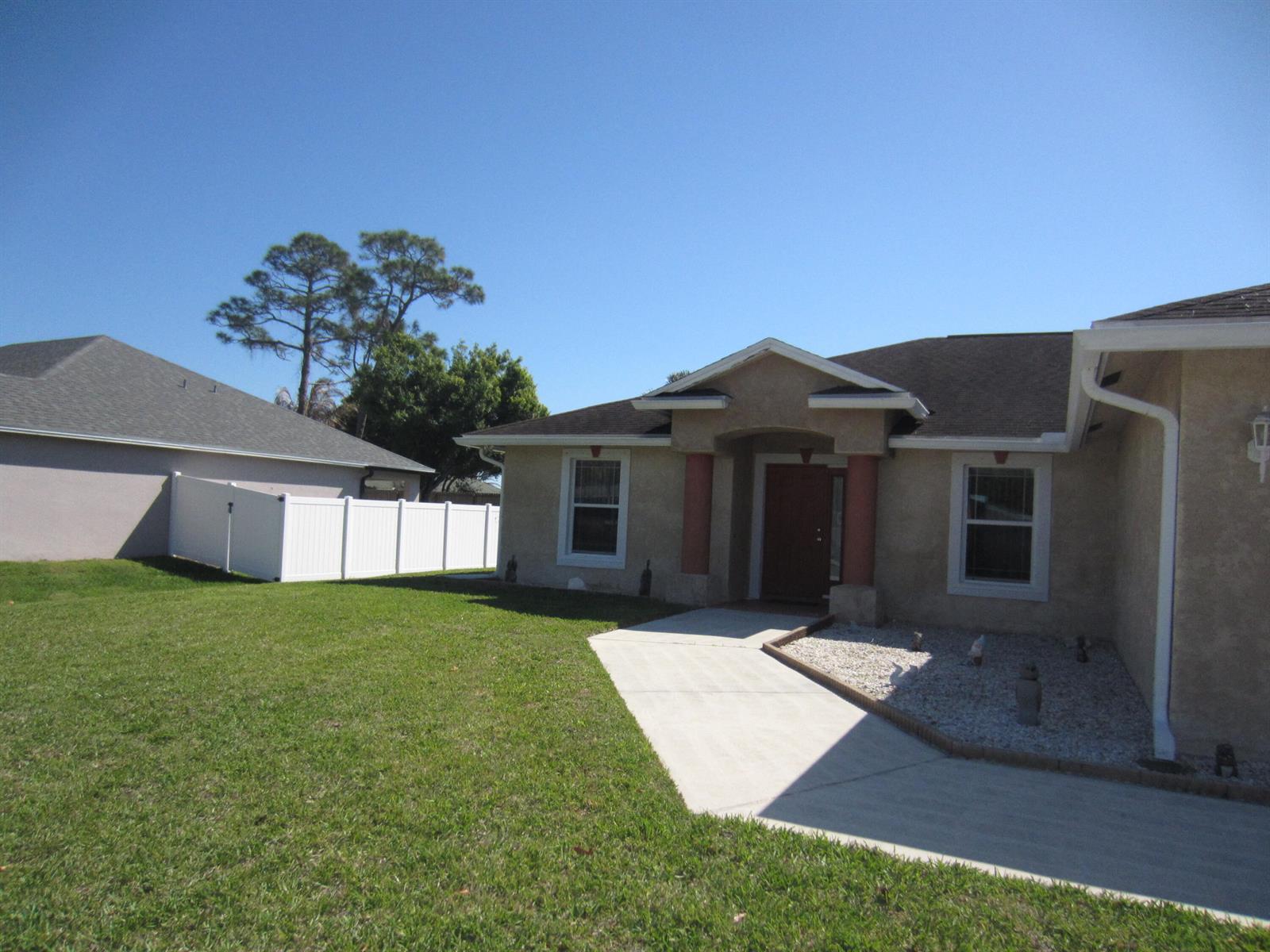 A tan single-story house features a front walkway, a white vinyl fence, and a lawn — 4702 Seagrape Drive, Fort Pierce FL 34982, FORT PIERCE, FL