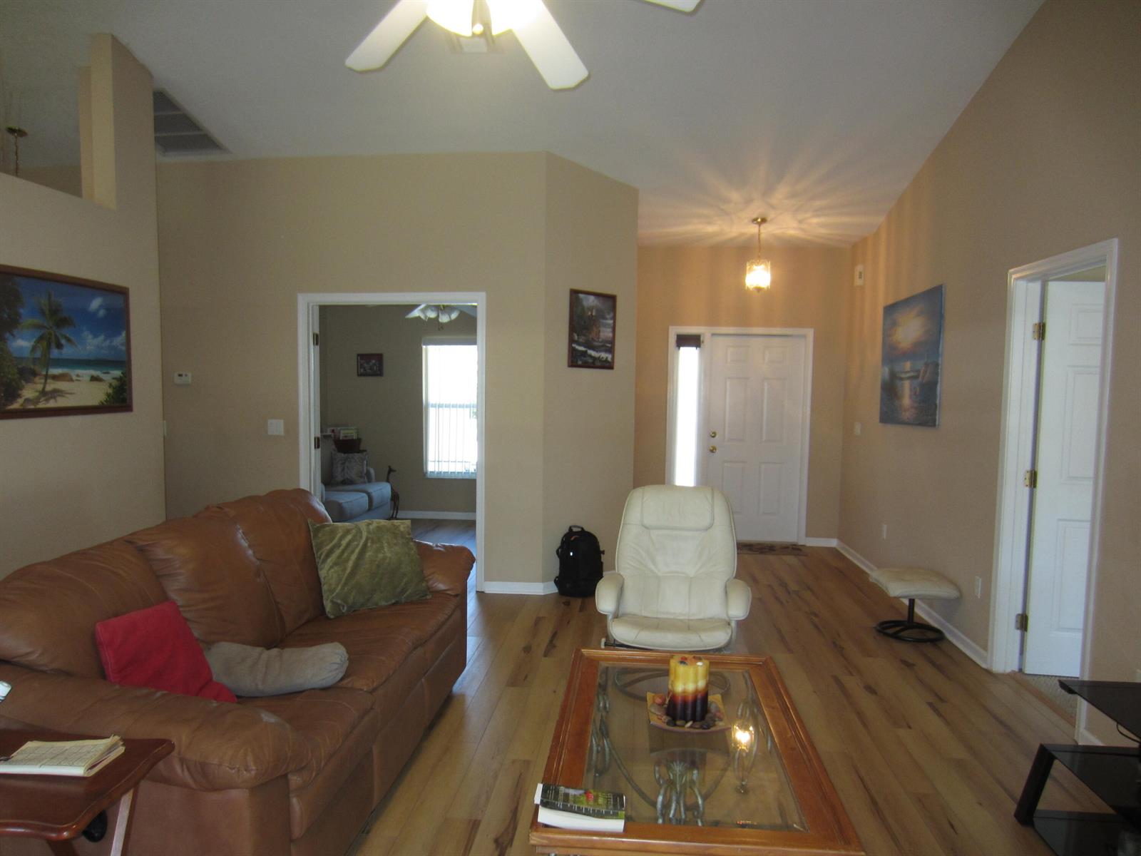 A living room features a brown leather sofa, white armchair, glass coffee table, and hardwood floors — 4702 Seagrape Drive, Fort Pierce FL 34982, FORT PIERCE, FL