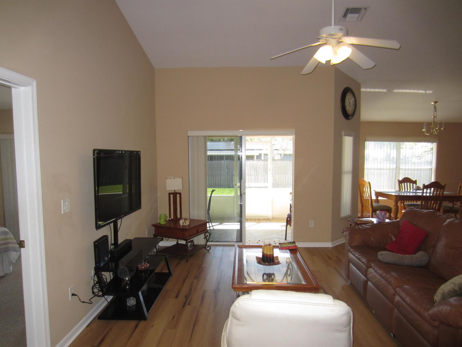 A living room with hardwood floors, a brown leather sofa, and a sliding glass door — 4702 Seagrape Drive, Fort Pierce FL 34982, FORT PIERCE, FL