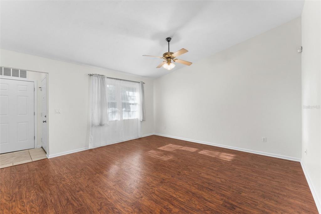 A living room features wood-look flooring, white walls, a ceiling fan, and a front door — 2026 SW 73RD STREET, GAINESVILLE, FL