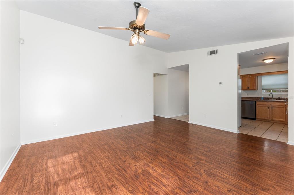 An empty living room with wood-look flooring, a ceiling fan, and an adjacent kitchen — 2026 SW 73RD STREET, GAINESVILLE, FL