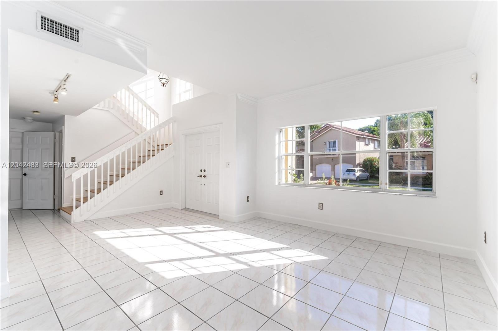 A bright, tiled living room features a staircase, white walls, and a large window — 4671 SW 154th Pl, Miami FL 33185, MIAMI, FL