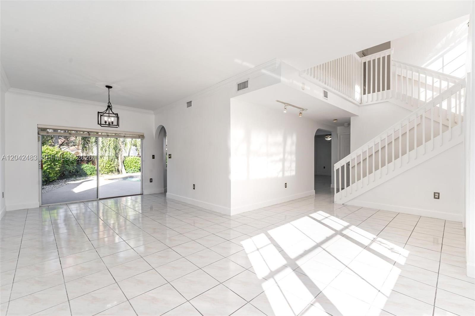 A bright, empty living room features white tile floors, a staircase, and sliding glass doors — 4671 SW 154th Pl, Miami FL 33185, MIAMI, FL