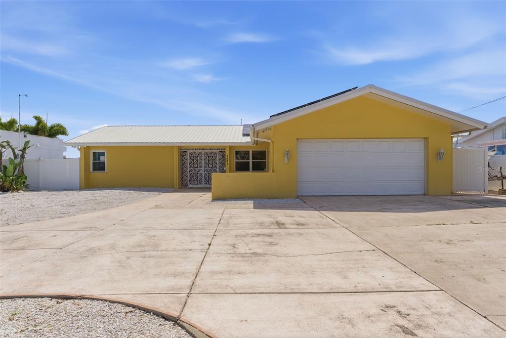 A yellow single-story house with a white metal roof and a large concrete driveway — 1421 SEA GULL DRIVE S, ST PETERSBURG, FL