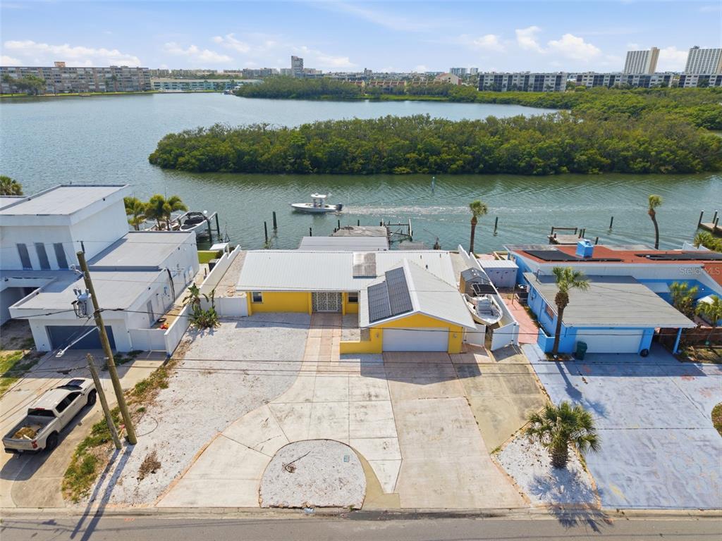 An aerial view of a yellow waterfront house with a concrete driveway and solar panels — 1421 SEA GULL DRIVE S, ST PETERSBURG, FL