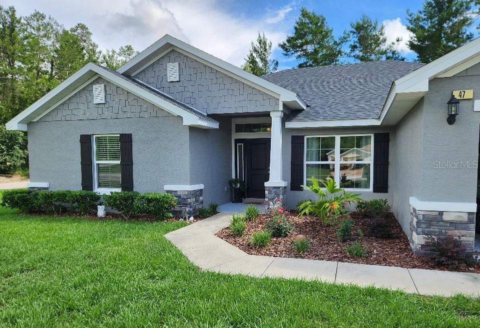 A gray single-story house features a stone-accented entryway, dark shutters, and a landscaped front yard — 47 VILLAGE CENTER DRIVE, HOMOSASSA, FL