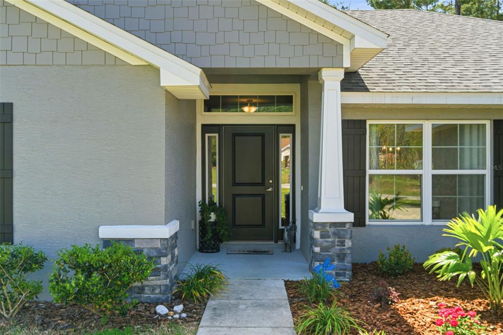 The exterior of a house features a gray front door, stone pillars, and shingled siding — 47 VILLAGE CENTER DRIVE, HOMOSASSA, FL