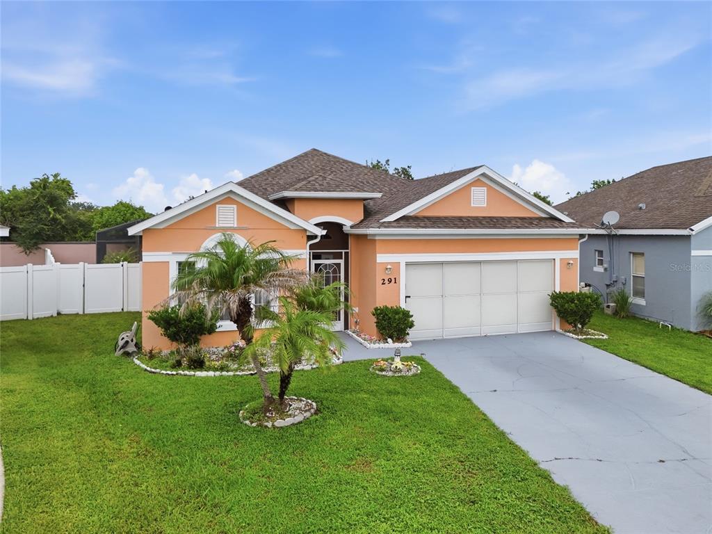 A single-story peach-colored house with a two-car garage and a front lawn — 291 MAGICAL WAY, KISSIMMEE, FL