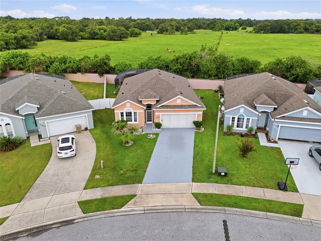 An aerial view shows three suburban houses with driveways and lawns bordering a large field — 291 MAGICAL WAY, KISSIMMEE, FL
