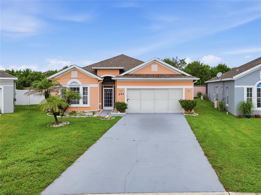 A single-story peach-colored house features a gray driveway, a two-car garage, and a front lawn — 291 MAGICAL WAY, KISSIMMEE, FL