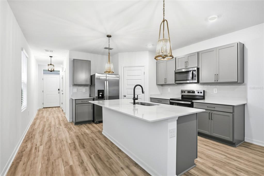 A modern kitchen features gray cabinets, white countertops, a central island, and light wood flooring — 5735 MOUNTAIN ROAD, DAVENPORT, FL