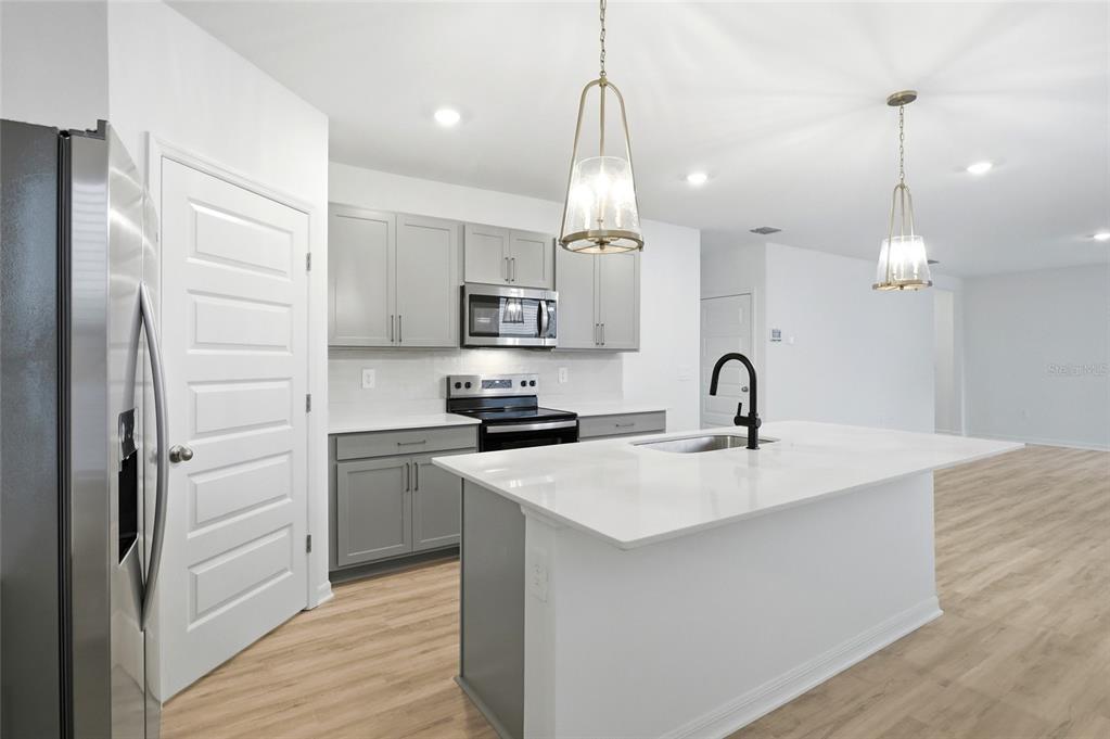 A modern kitchen features gray cabinets, white countertops, a central island, and stainless steel appliances — 5735 MOUNTAIN ROAD, DAVENPORT, FL