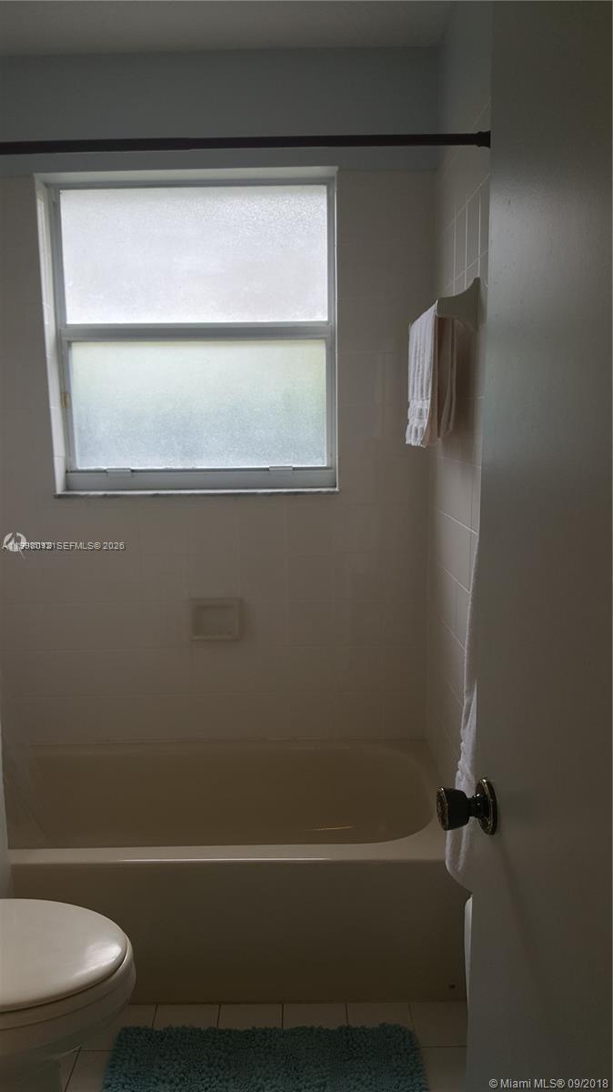 A bathroom features a bathtub, a window with frosted glass, and white wall tiles — 15989 SW 149th Ter # 15989, Miami FL 33196, MIAMI, FL