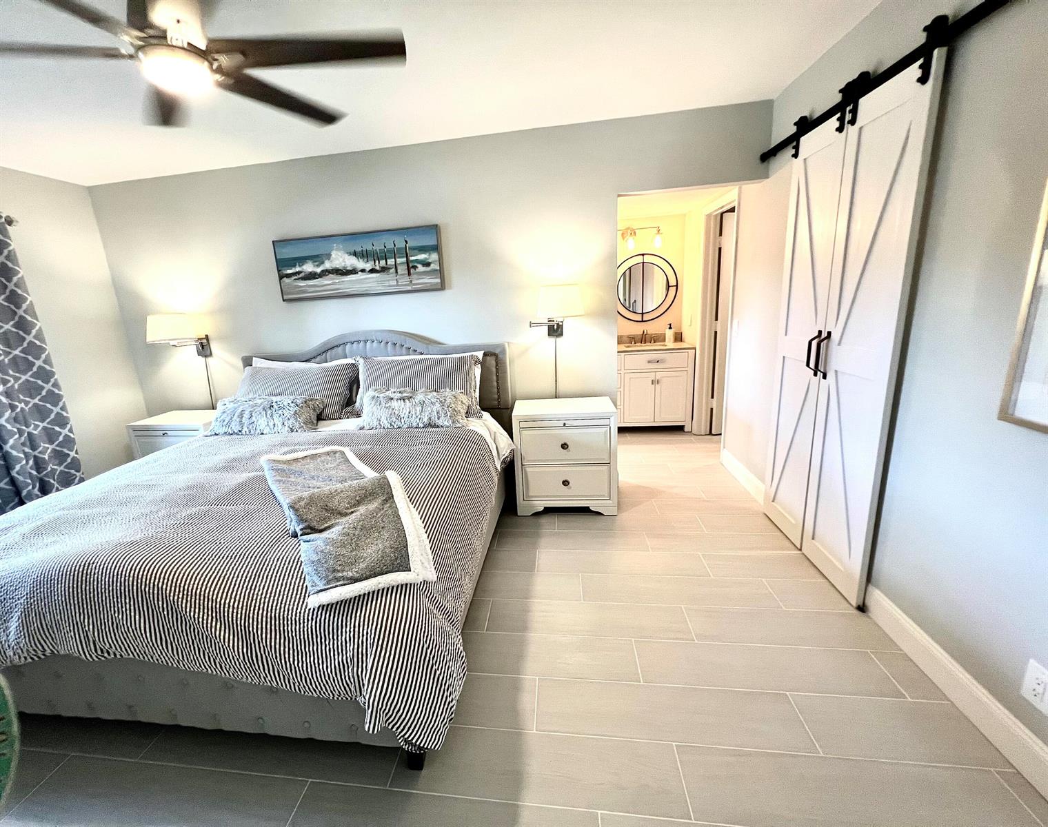 A bedroom features a striped bed, gray tile flooring, and a white barn door — 17081 Waterbend Dr Drive Unit 229, Jupiter FL 33477, JUPITER, FL